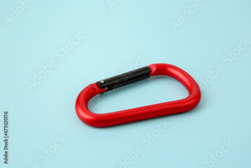 One red carabiner on light blue background, closeup