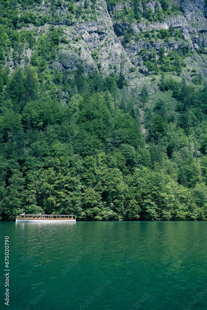 Fototapeta premium Boat sailing across Koenigssee Lake surrounded by lush mountains and verdant trees in Germany