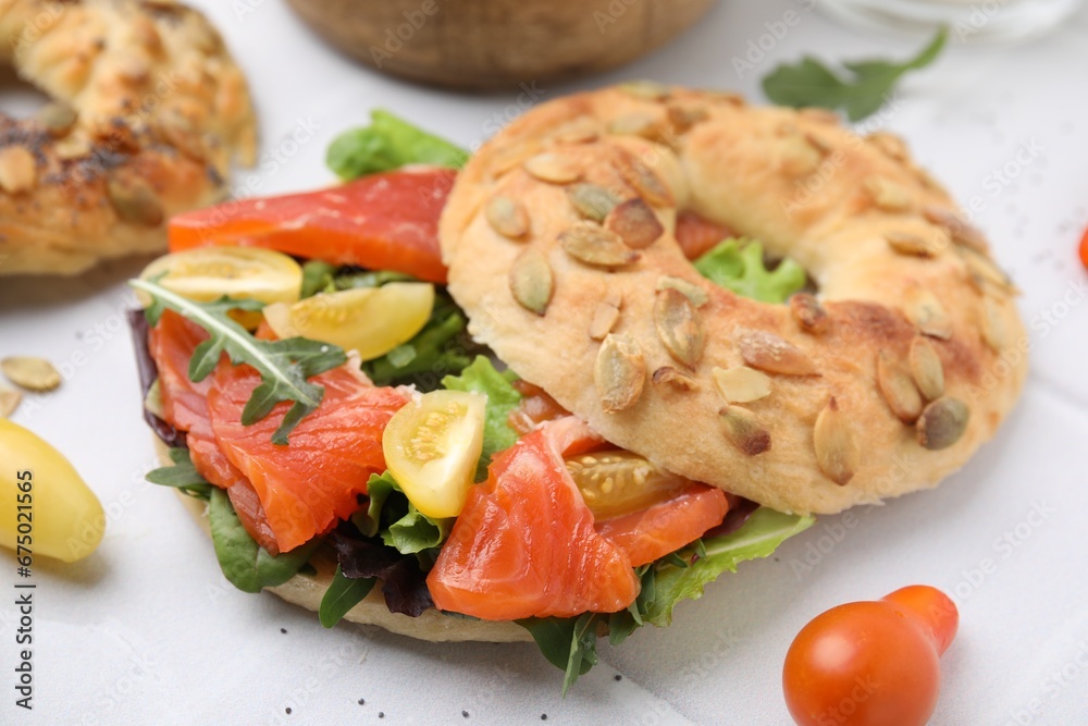 Tasty bagel with salmon, lettuce, tomatoes and arugula on white tiled table, closeup Tasty bagel with salmon, lettuce, tomatoes and arugula on white tiled table, closeup