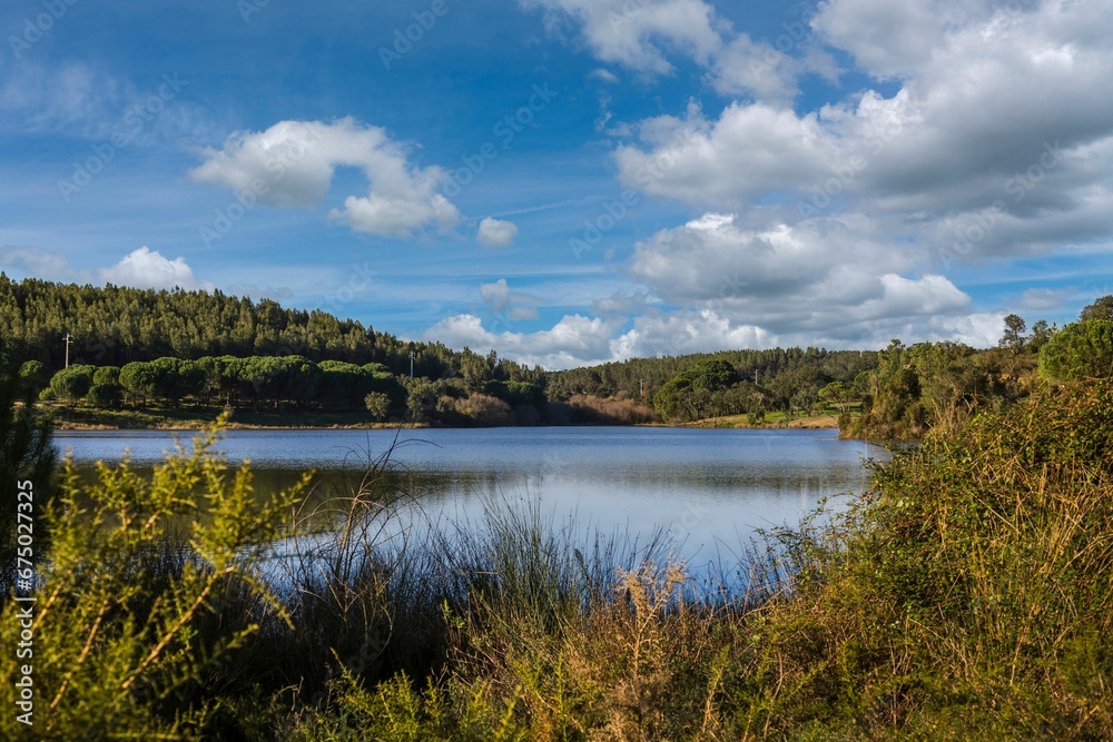 Fototapeta premium Lake in the woods with beautiful winter blue skies reflections. Bricks water dam in a small village