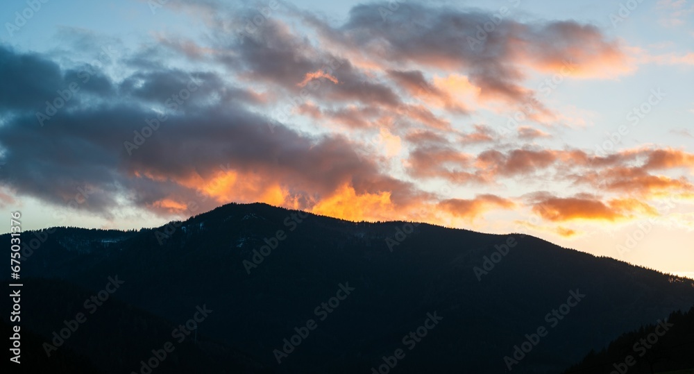 a silhouette of a mountain against the sky with clouds at sunset