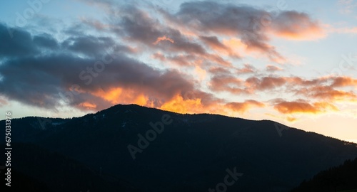 a silhouette of a mountain against the sky with clouds at sunset
