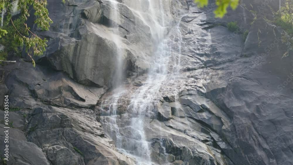 Landscape scene of flowing waterfall on gray rocky cliff with green tree leaves