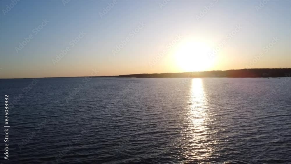 Aerial of the golden sunset shining over the calm blue sea with hills in the background Aerial of the golden sunset shining over the calm blue sea with hills in the background