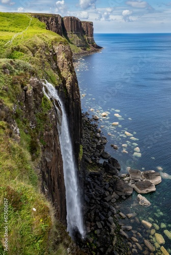 a waterfall pouring into the ocean from a hill with green grass