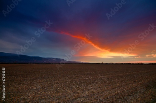 Desolate landscape with a barren field and an overcast sky with thick clouds © Wirestock