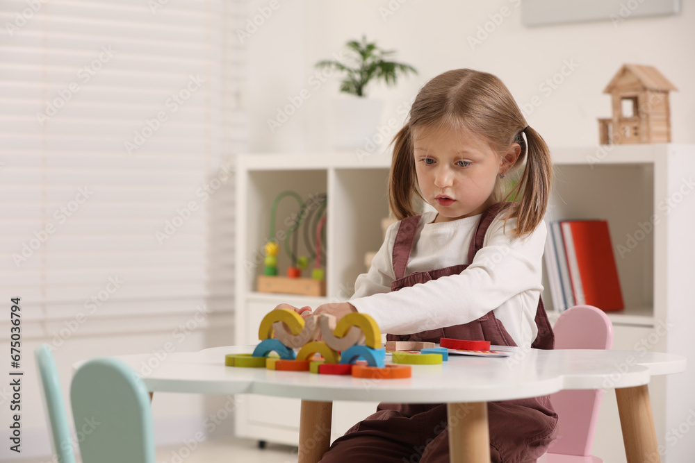 Cute little girl playing with colorful wooden pieces at white table indoors, space for text. Child's toy