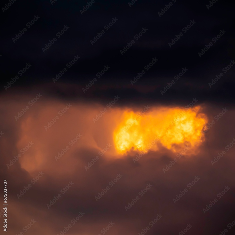 orange and yellow light coming through clouds and on a dark sky orange and yellow light coming through clouds and on a dark sky