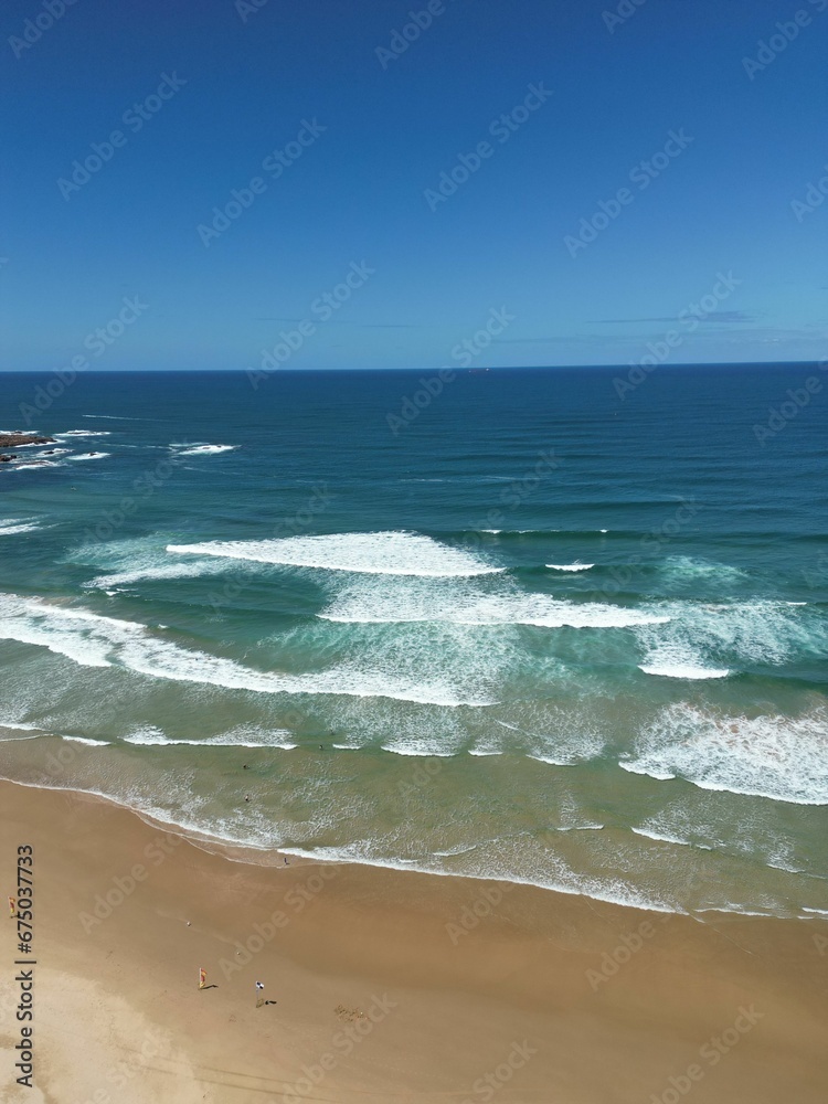 Aerial view of sandy beach with clear blue ocean and blue sky in the background
