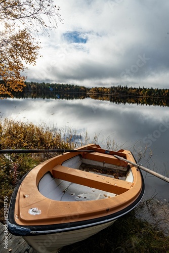 Fototapeta Naklejka Na Ścianę i Meble -  Boat is perched on the water's edge of a tranquil lake surrounded by golden autumn foliage