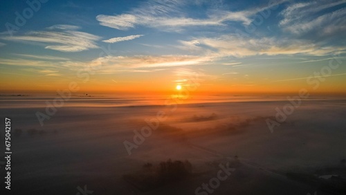 Aerial view of breathtaking landscape of the sun setting behind a rolling blanket of fog © Wirestock