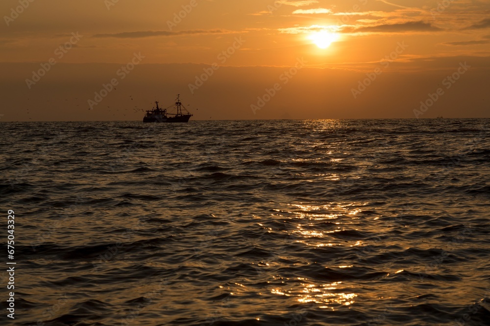 Tranquil beach scene with a majestic sunset sky, featuring a silhouetted sailing vessel in distance
