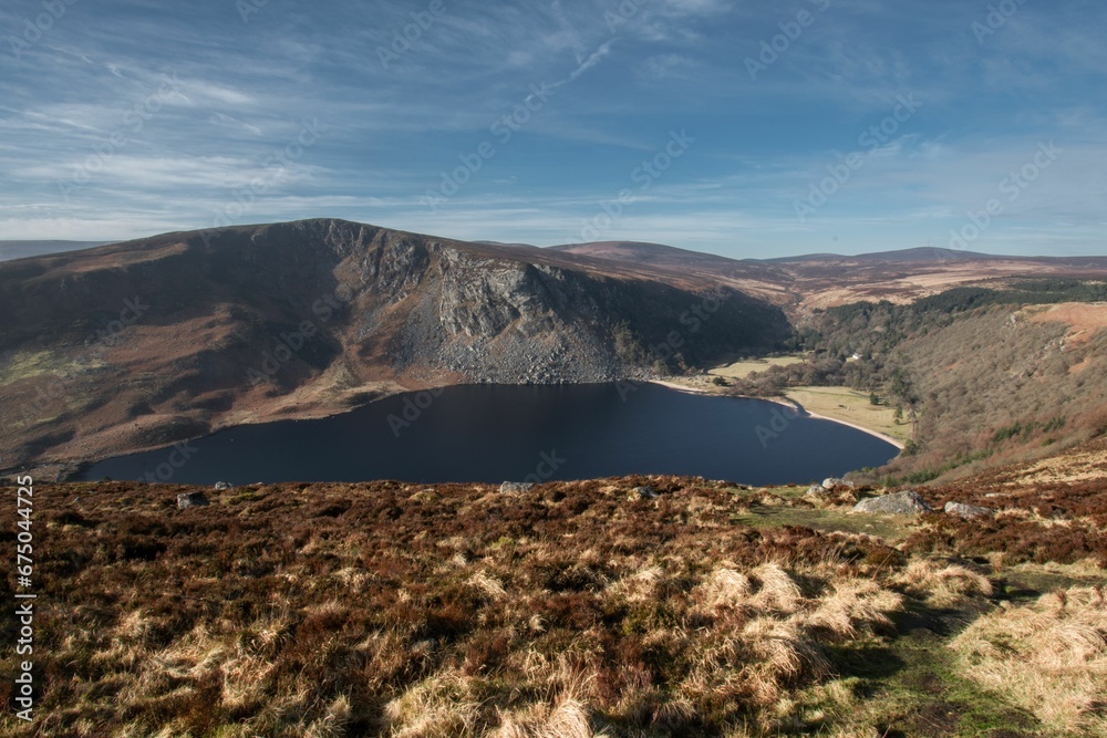 Stunning view of the Lough Tay lake surrounded by lush vegetation under the cloudy blue sky