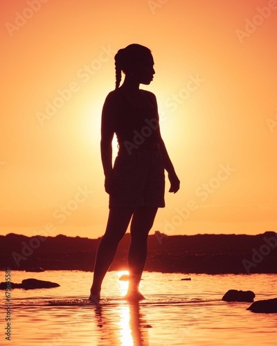 Woman s silhouette standing in the shallow waters at the edge of a beach at sunset