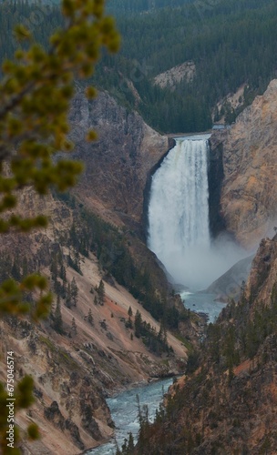 a waterfall casing through a valley surrounded by mountains and pine trees