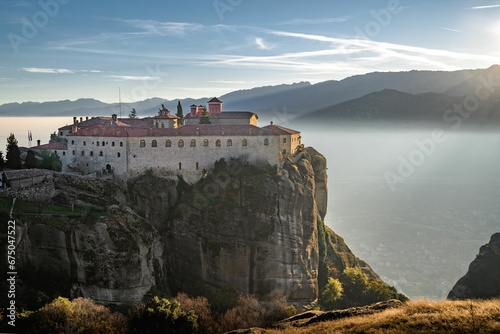 Fototapeta Naklejka Na Ścianę i Meble -  Historic monastery atop a mountain cliff, overlooking a tranquil lake in Meteora, Greece.