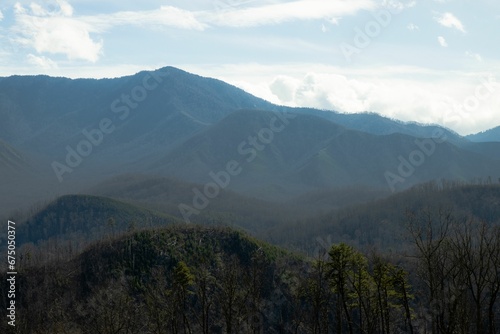 Breathtaking image of a mountain range is blanketed with lush green trees and wispy white clouds