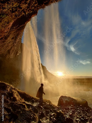 a man standing at the base of a waterfall by a cliff