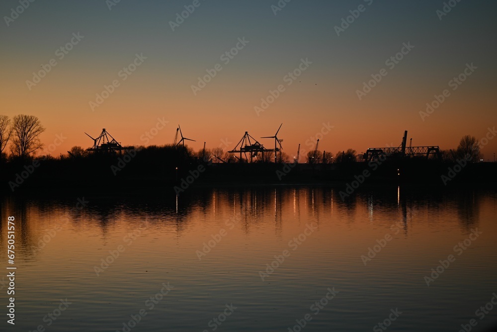 Stunning sunset scene of a river with trees and wind turbines silhouette in the backdrop