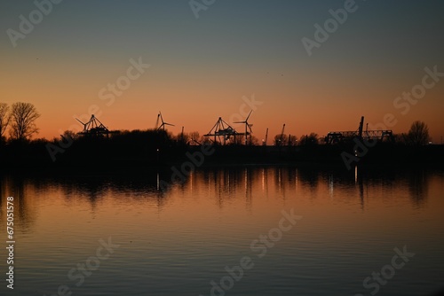 Stunning sunset scene of a river with trees and wind turbines silhouette in the backdrop