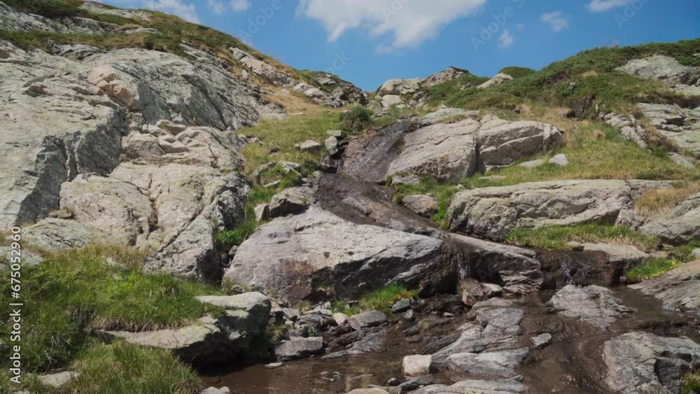 View of small waterfalls on a rocky mountain with blue cloudy sky View of small waterfalls on a rocky mountain with blue cloudy sky