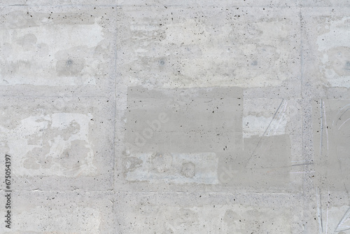 A weathered and cracked concrete wall with smooth surface texture, light to medium grey colors, and splotchy square marks photo