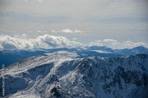 Ridges of the Retezat Mountains surrounded by clouds and blue sky. © Wirestock