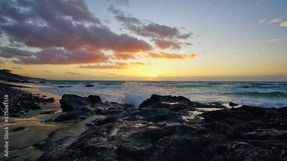 Stunning view of the sun setting over the ocean from a beach area, with rocks in the foreground