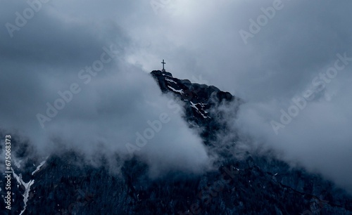 Scenic view of a cross on top of a snow-capped mountain on a cloudy day