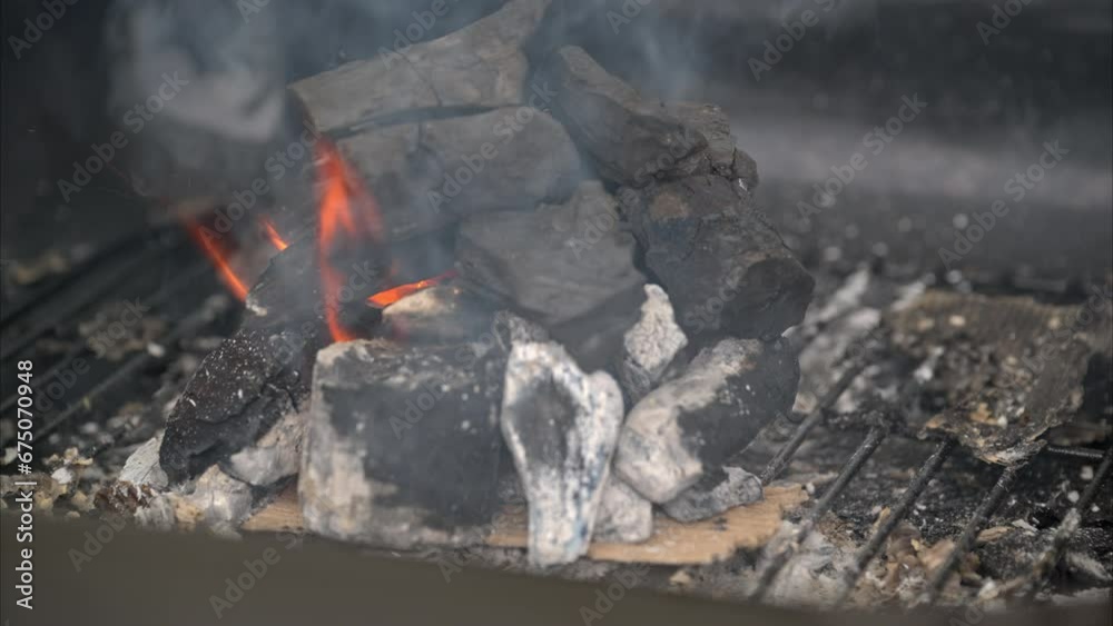 Slow motion of a fire starting using charcoal on a grill with smoke an flames coming out due to the wind Slow motion of a fire starting using charcoal on a grill with smoke an flames coming out due to the wind