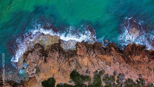 Aerial shot of a beach with crystal-clear blue water surrounded by rocks and lush green trees.