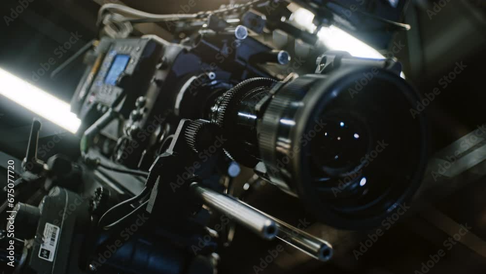Low angle shot of a professional cinema camera and long telephoto zoom lens, remote device is turning the gears and the lens element is moving to change focal length. Focus on zoom motor. Low angle shot of a professional cinema camera and long telephoto zoom lens, remote device is turning the gears and the lens element is moving to change focal length. Focus on zoom motor.