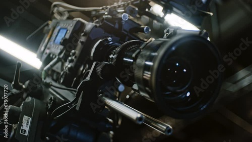 Low angle shot of a professional cinema camera and long telephoto zoom lens, remote device is turning the gears and the lens element is moving to change focal length. Focus on zoom motor.