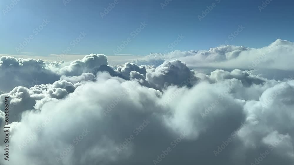 A pilot’s perspective flying over a stormy sky full of cumulus clouds. 10000m high. Daylight, sunny, with a deep blue sky.