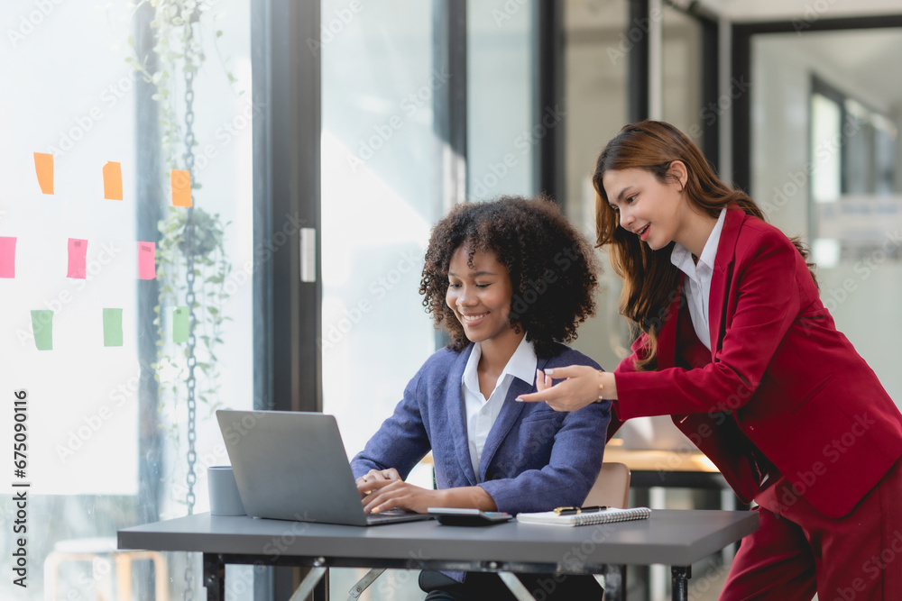 Two happy businesswoman talking and consulting working together in the office. Businesswoman discussing with colleague over laptop at desk in office. Two happy businesswoman talking and consulting working together in the office. Businesswoman discussing with colleague over laptop at desk in office.