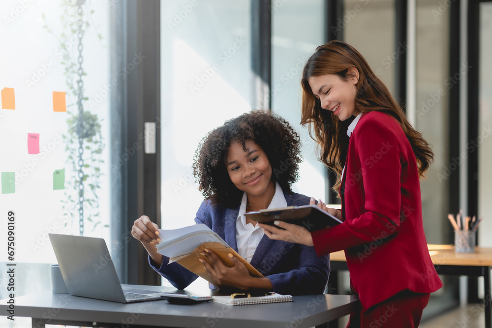 Two happy businesswoman talking and consulting working together in the office. Businesswoman discussing with colleague over laptop at desk in office. Two happy businesswoman talking and consulting working together in the office. Businesswoman discussing with colleague over laptop at desk in office.