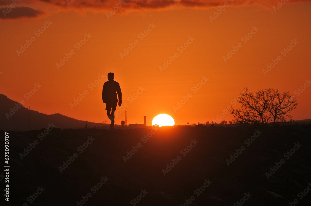 Silhouette of a man on the beach at sunrise.