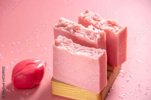 Cute pink pieces of organic eco soap on a soap dish made of natural wood on a pink background. Concept of modern and safe cosmetic products for skin care