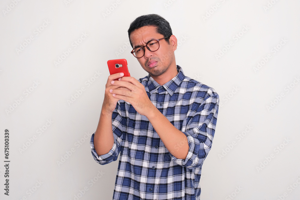 Adult Asian man looking to his phone with sad expression Adult Asian man looking to his phone with sad expression