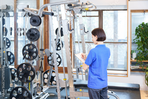 スポーツジムのトレーニングマシンを点検する女性スタッフ