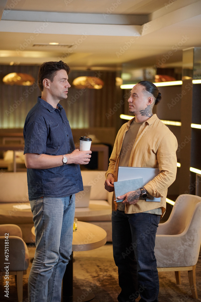 Serious businessmen discussing project development in office lounge area Serious businessmen discussing project development in office lounge area