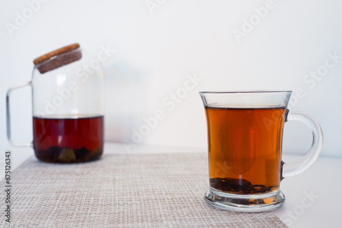 Black tea in a glass cup and glass teapot freshly brewed on a napkin with white background