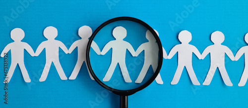 Abstract paper figures of people under black magnifying glass on a blue background photo