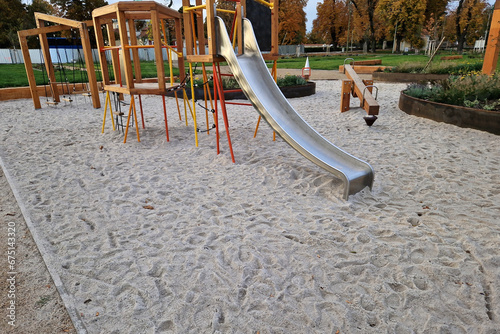 crawling wooden attraction on the sandpit. children have a stainless steel slide and rope nets for climbing and for greater safety on the bridge. stone sandstone wall in the background of kindergarten