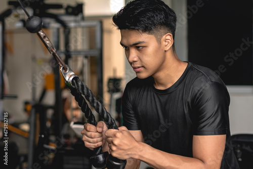A typical young asian man does a set of tricep pushdowns at an open-air gym.