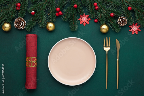 Clean empty plate, golden cutlery. Festive table setting with christmas decorations. Celebration xmas eve, flat lay. Red, gold and green accents. Fir cones on evergreen tree. Holiday banquet, top view