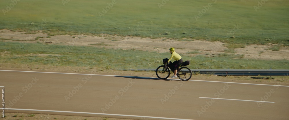 Obraz premium The woman traveler on bike on an asphalt winding road. The picturesque top view. The girl journey on touring bike with bikepacking bags