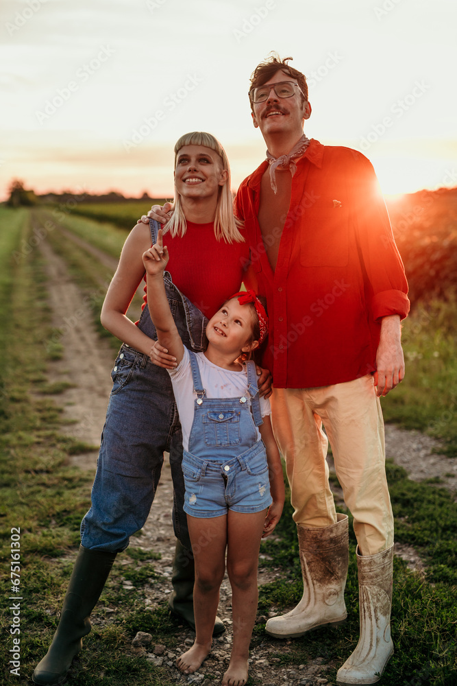 A mom, dad, and their daughter walking together, smiling and basking in the tranquil countryside as the sun sets after a long day's work