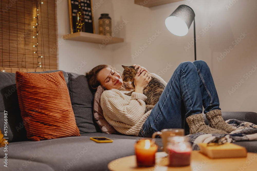 Cozy at home with tabby cat, woman with her pet on sofa ay home in evening