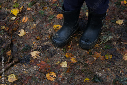 Close up of toddlers rain boots, ground with autumn yellow leaves 
